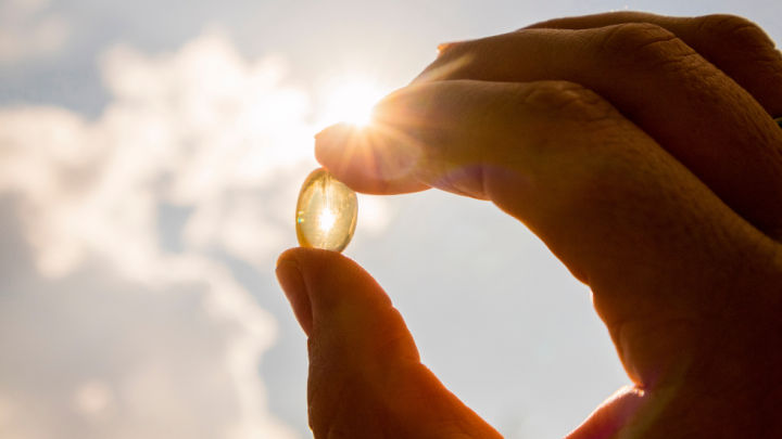 Outdoor closeup of fingers holding a translucent pill up to bright sunlight